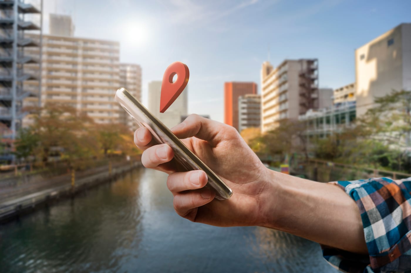 Main tenant un smartphone avec une épingle de géolocalisation rouge flottante sur fond de ville